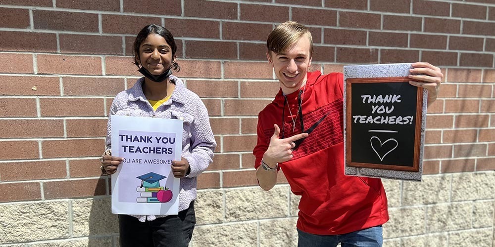 Two students hold thank you teacher signs