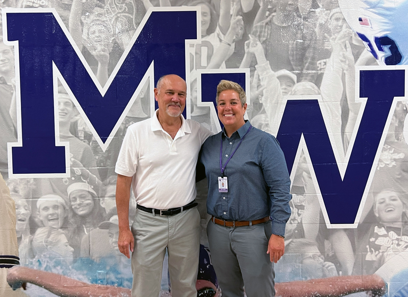 Mr. Dimmit and Lori Hock, Asst. Supt for HR, stand in front of the hallway mural featuring his photos through the years. 